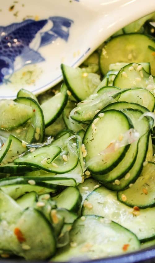 marinated asian cucumber salad with rice vinegar next to a blue and white spoon rest.