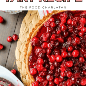Overhead view of a cranberry tart with a golden crust on a woven mat, surrounded by fresh cranberries and a bowl of cranberry sauce. Text reads: Cranberry Tart Recipe - The Food Charlatan.