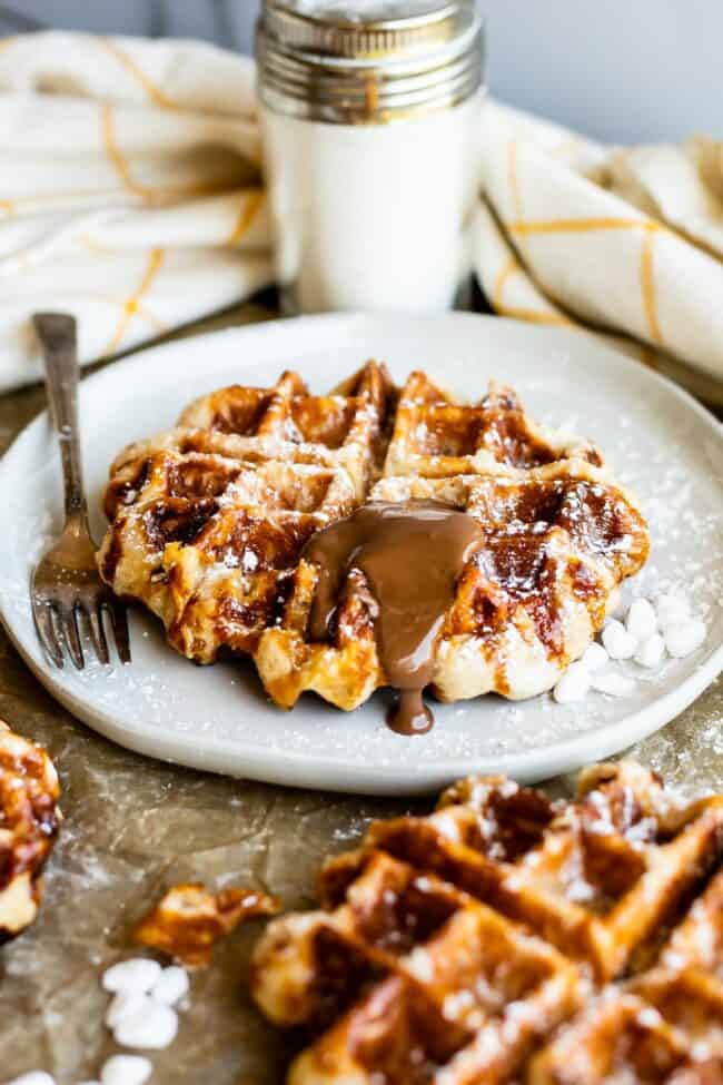 liege waffles on a plate with nutella melting on top and pearl and powdered sugars nearby.