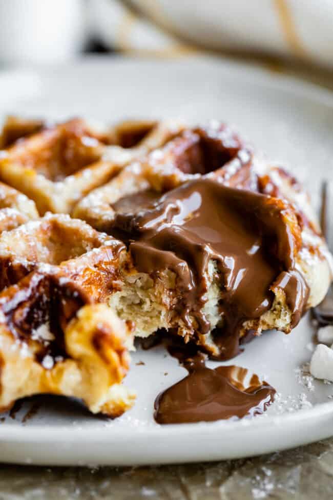 a liege waffle on a plate with nutella melting on top and pearl sugar nearby.