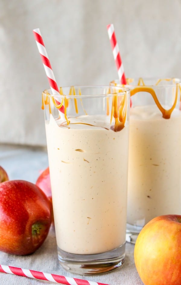 Caramel Apple Cider Reduction Shake in a clear glass with caramel drizzels, straws and apples. 