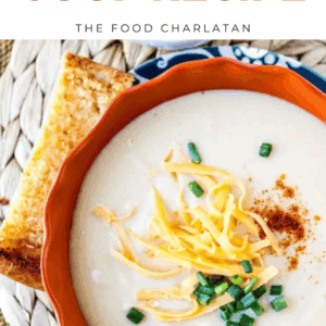 A bowl of creamy cauliflower soup topped with shredded cheddar cheese, chopped chives, and paprika, served with a slice of toasted bread. Text above reads Cheddar Cauliflower Soup.