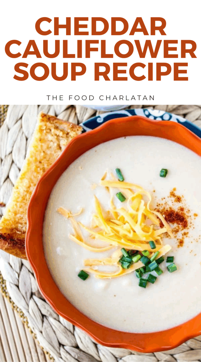 A bowl of creamy cauliflower soup topped with shredded cheddar cheese, chopped chives, and paprika, served with a slice of toasted bread. Text above reads Cheddar Cauliflower Soup.