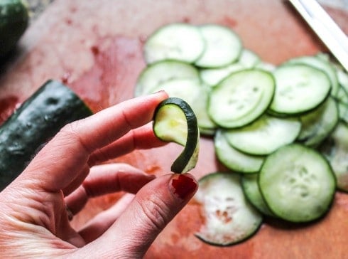 hand showing the flexibility of a thin cucumber slice.