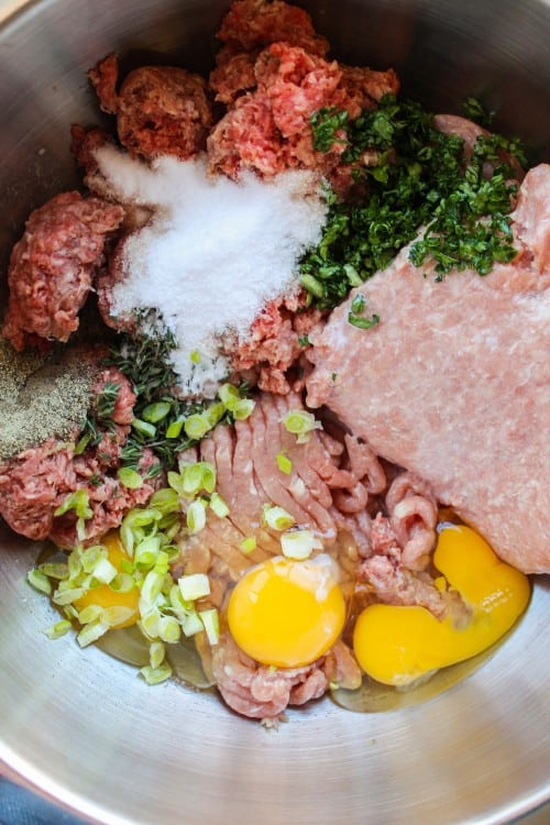 ground beef, eggs, celery, onions, fresh herbs, and spices in a metal bowl for making meatloaf.