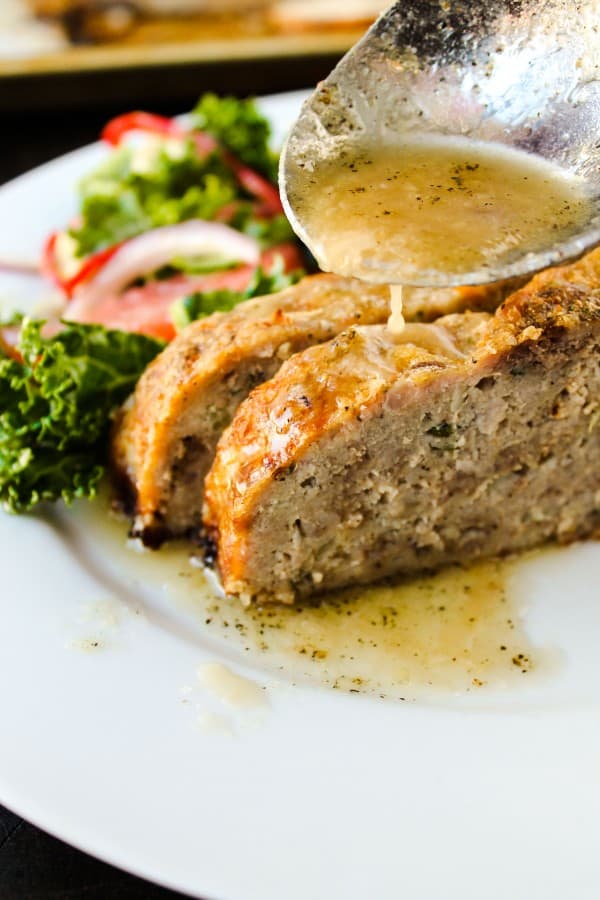 slices of meatloaf being drizzled with garlic sauce and a side salad on a plate. 