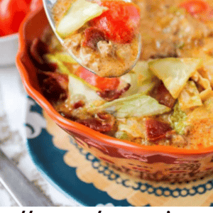 A spoon lifts a portion of cheeseburger soup from a bowl, with chunks of tomato, cheese, and meat in a creamy broth. The text reads: The most amazing cheesy cheeseburger soup. The Food Charlatan.