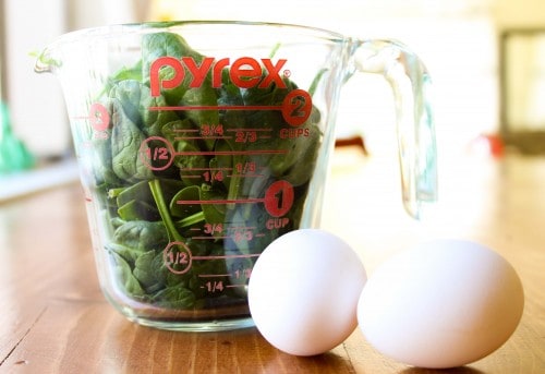 a measuring cup of spinach and two eggs.