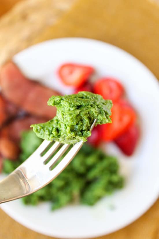 a forkful of green eggs against a background of green eggs, ham, and strawberries on a white plate.