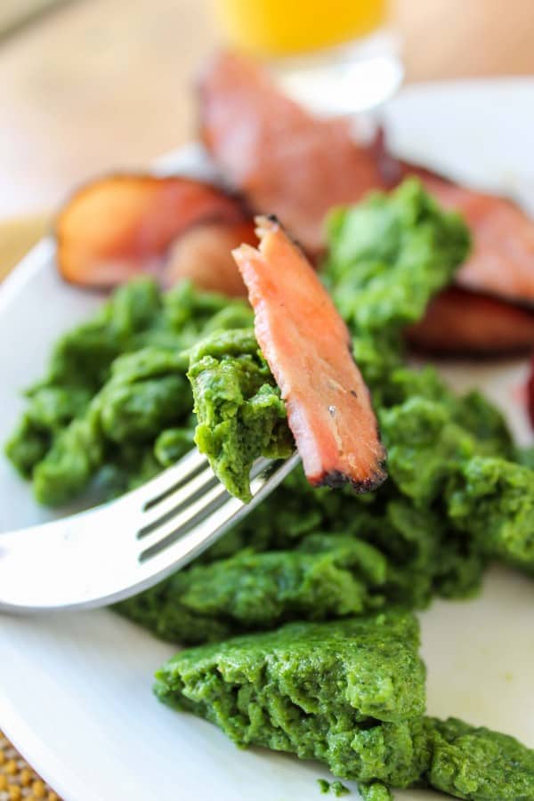 green eggs made with spinach and black forest ham on a white plate with a fork. 