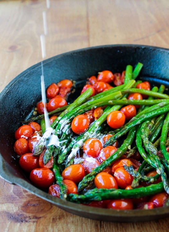 cream dripping into a cast iron pan of asparagus and cherry tomatoes.