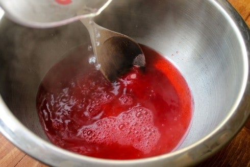 Pouring boiling water into bowl with strawberry gelatin mix.