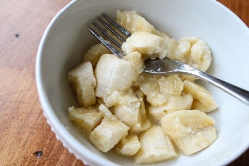 Mashing bananas in a white bowl with a fork.