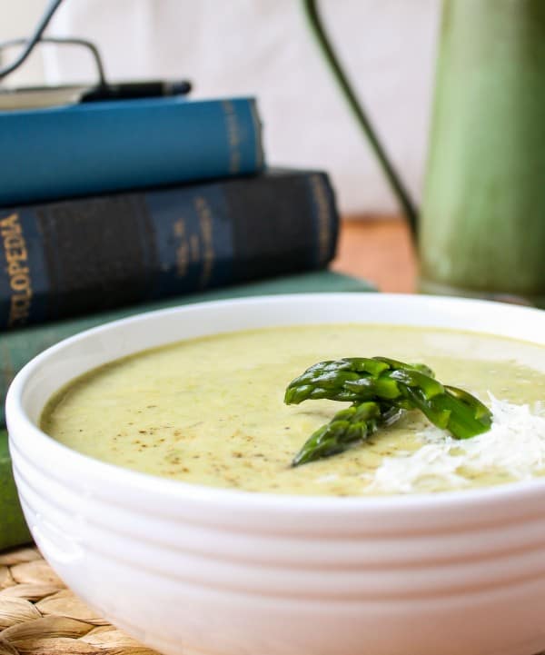 a bowl of asparagus soup with a stack of vintage books and a pair of glasses. 