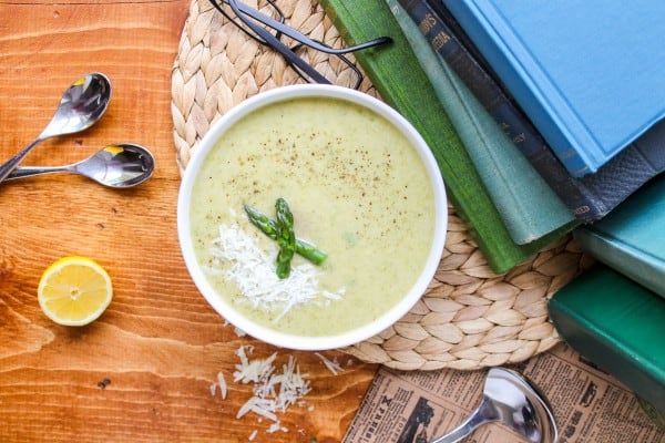 asparagus soup shot from above with spoons, a half lemon, and books.