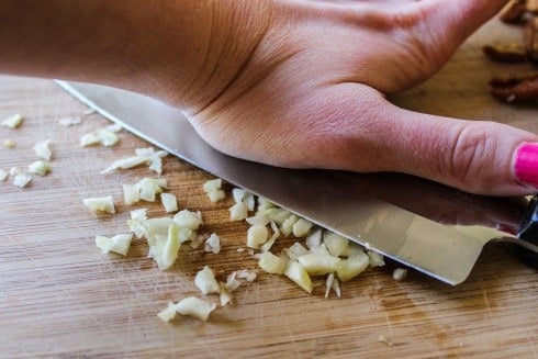 smashing garlic on a wooden cutting board.