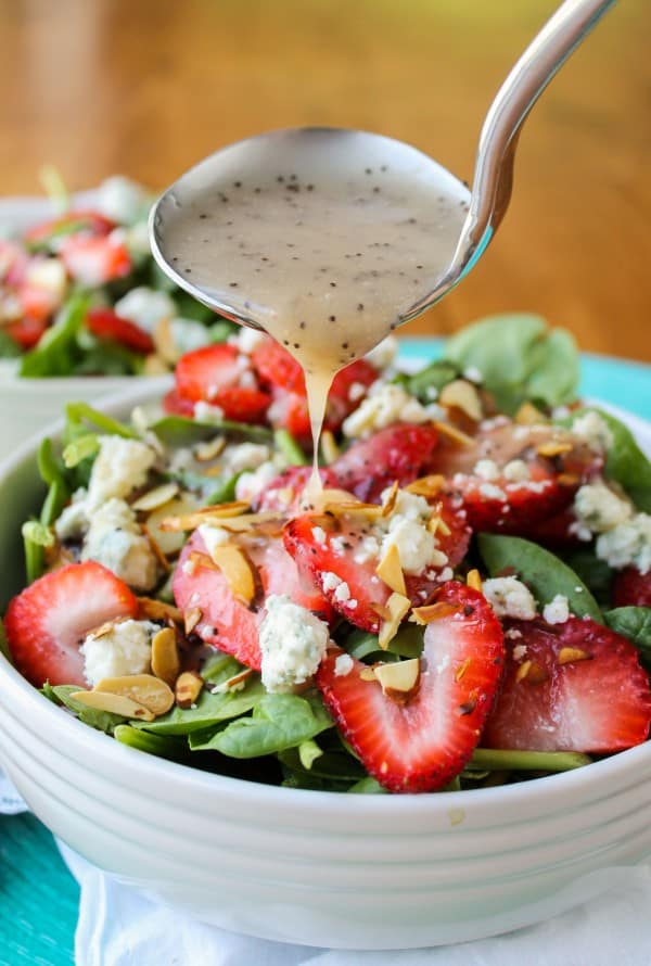 Strawberry bleu cheese salad in white bowl with poppyseed dressing drizzling out of ladle.
