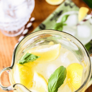A glass pitcher filled with basil lemonade, ice, and lemon wedges, topped with the text Super Simple BASIL LEMONADE.