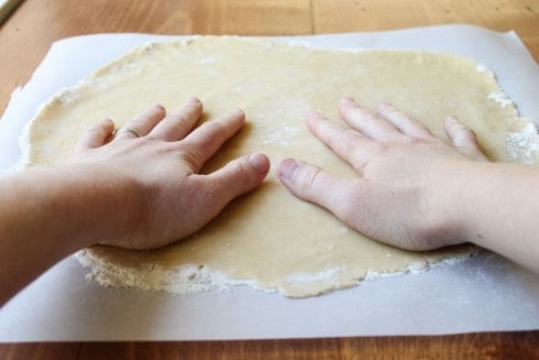 hands patting a rolled out pie crust. 