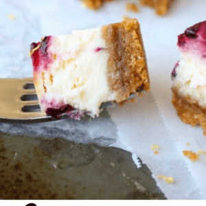 A fork holds a square piece of cheesecake bar with a graham cracker crust, creamy filling, and blackberry and lemon topping. Another dessert sits in the background on parchment paper. Text reads: Cheesecake Bars with Blackberry & Lemon.