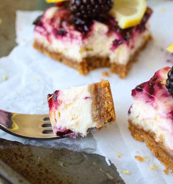 blackberry lemon cheesecake bars on parchment paper with a bite on a fork.