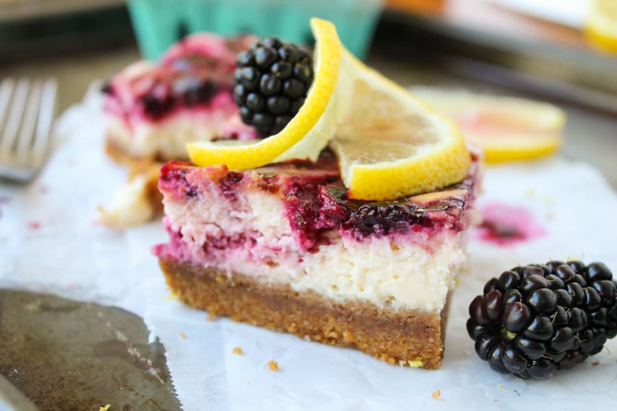 a close up shot of a blackberry lemon cheesecake bar on parchment paper. 