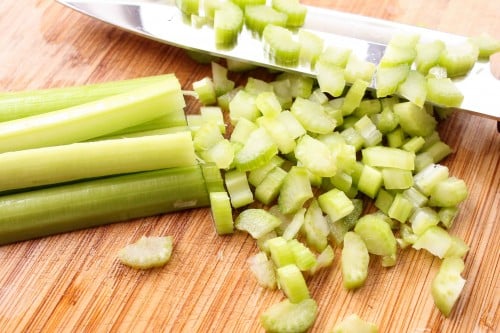 celery being chopped on a wooden cutting board.