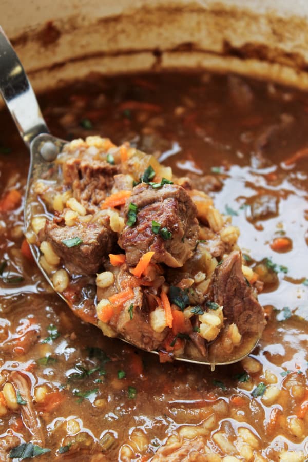 beef barley crock pot soup being lifted from a pot. 