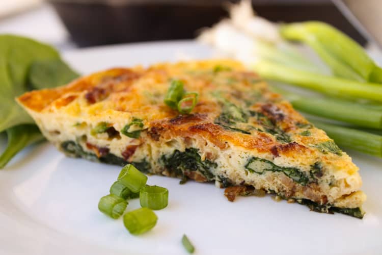 Bacon frittata on a plate with green onions.