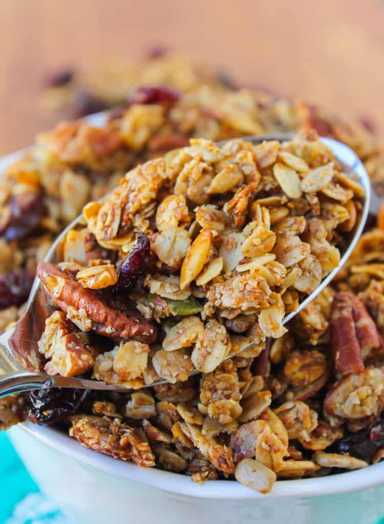 maple granola with pecans and cherries in a spoon above a white bowl of granola. 