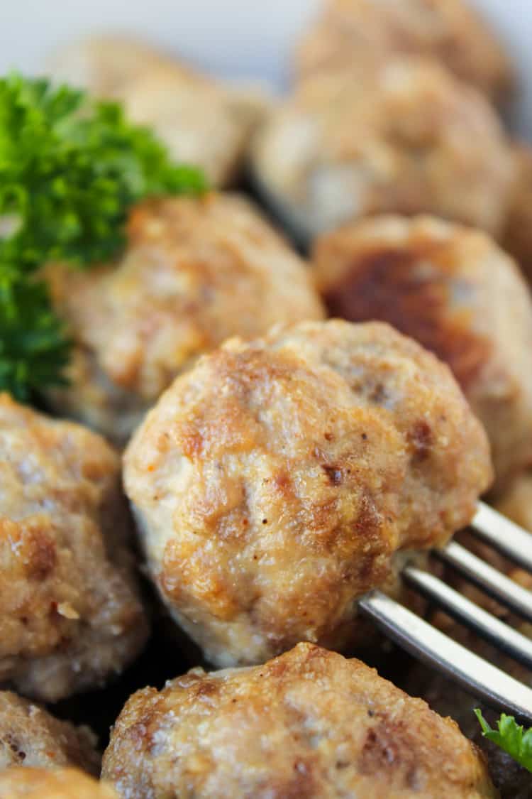 a fork spearing a baked meatball with parsley garnish. 