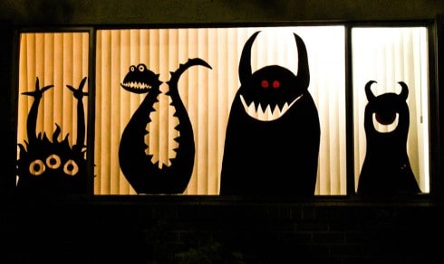 construction paper cutout monsters in a lit window at night. 