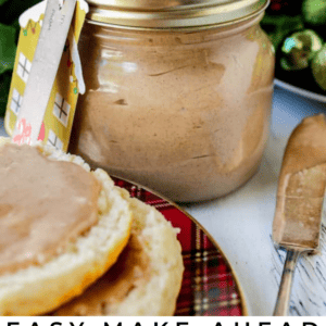 A jar of cinnamon honey butter with a gift tag sits on a table next to a plate with a biscuit spread with the creamy butter. Holiday greenery and a butter knife add festive flair, while text reads: “Easy Make-Ahead Cinnamon Honey Butter.”.