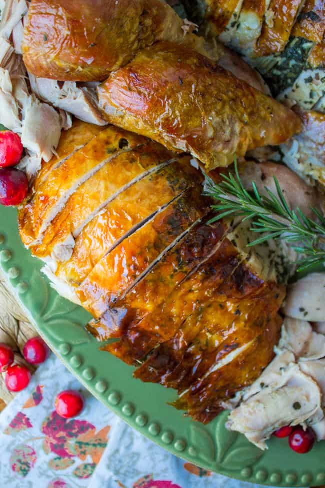 sliced roast turkey with rosemary and fresh cranberries on a green platter.
