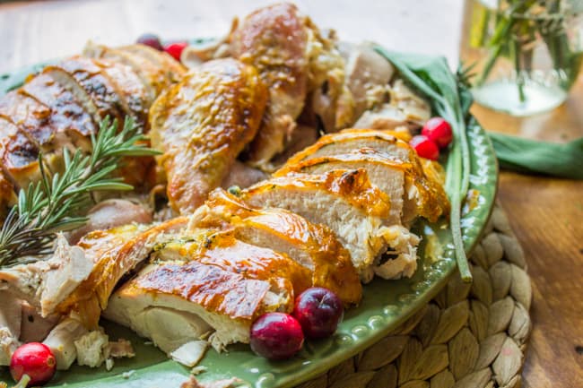 Carved up roasted turkey on platter with rosemary and cranberries. 