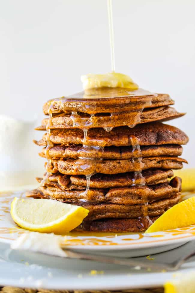 a tall stack of gingerbread pancakes drizzled with lemon syurp, served with lemon slices on a plate.