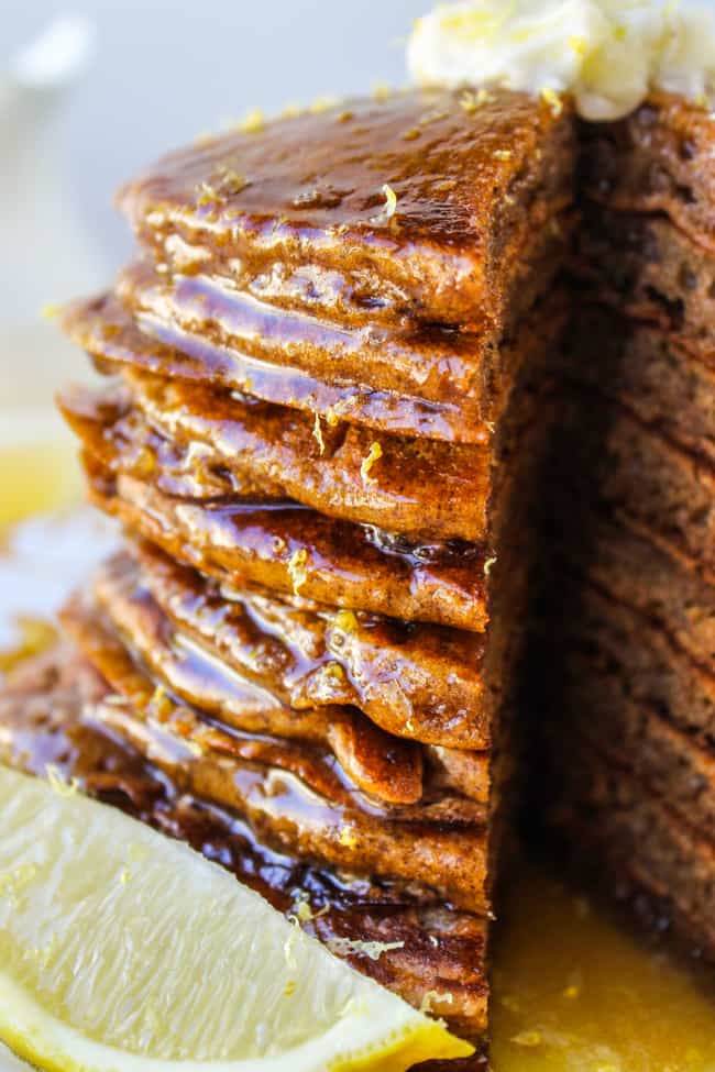 a tall stack of gingerbread pancakes with a slice cut out, drizzled in lemon syrup. 