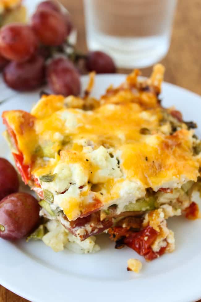 egg, bacon, and asparagus casserole on a plate with grapes.