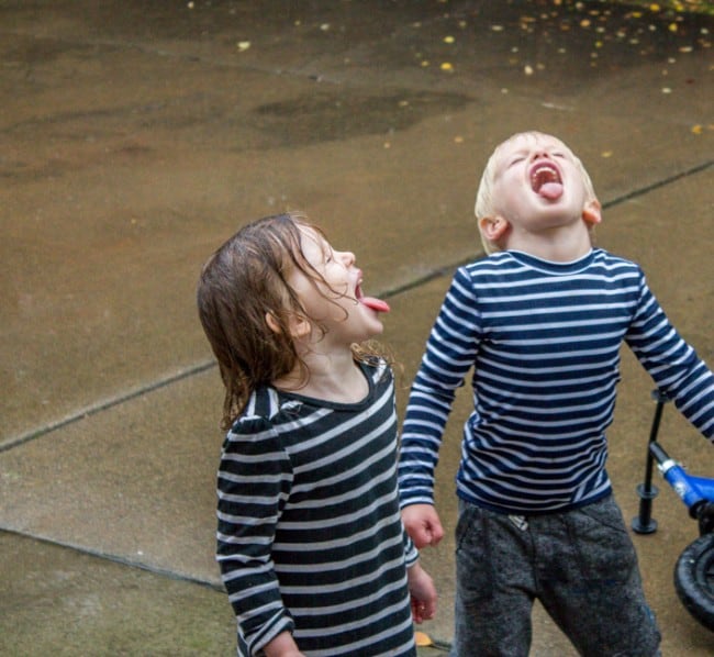 two children in striped shirts sticking their tongues out to catch raindrops.