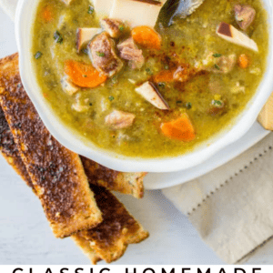 A bowl of split pea soup with smoked gouda cheese, served alongside toasted bread. The hearty soup features carrots, ham, herbs, and a bay leaf for rich flavor.