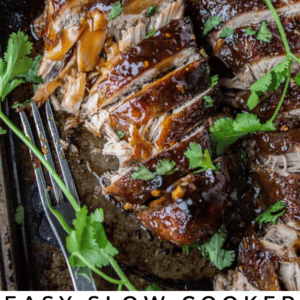 Sliced, glazed pork tenderloin garnished with fresh cilantro on a baking tray, with lime wedges and a fork beside it. Text overlay reads: Slow Cooker Asian-Inspired Pork Tenderloin - The Food Charlatan.