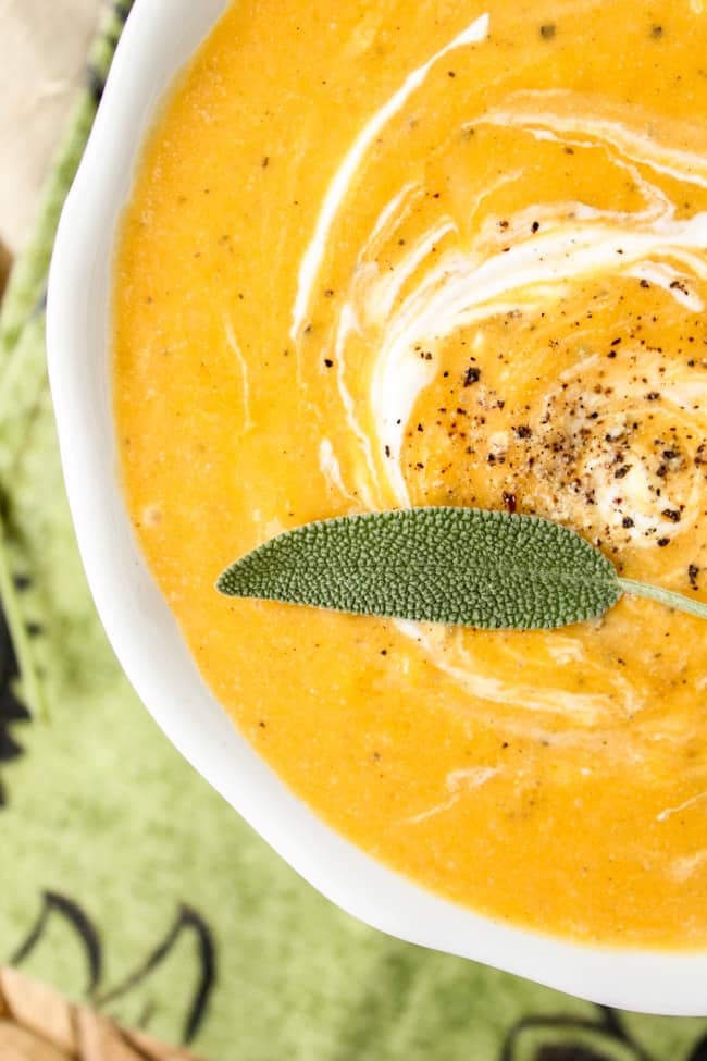 a close up shot of a bowl of butternut squash with cream, fresh pepper, and fresh sage. 