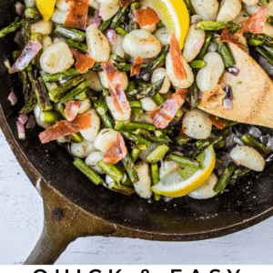 a cast iron skillet with gnocchi, asparagus, lemon slices, and a wooden spoon.