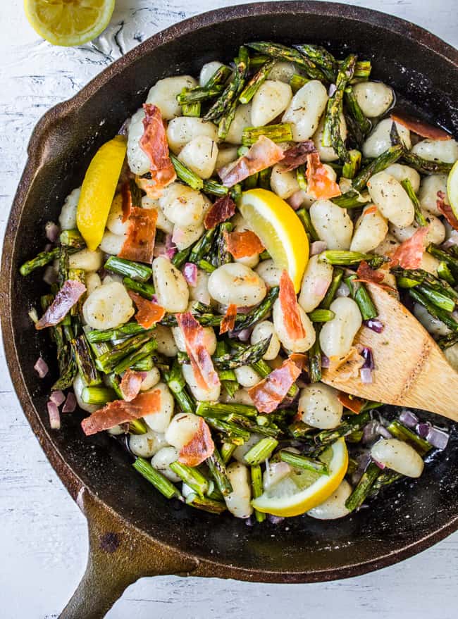 a cast iron pan with gnocchi, lemon slices, asparagus, and prosciutto. 