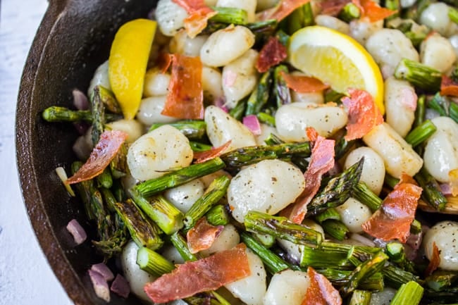 a cast iron pan of gnocchi, lemon slices, asparagus, and prosciutto.