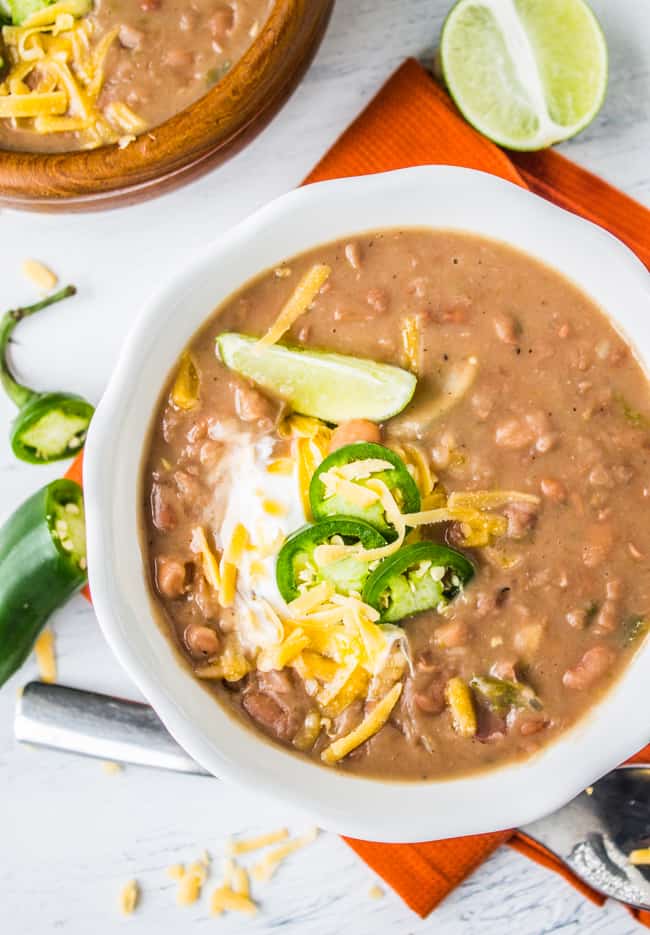 overhead shot of a bowl of Mexican pinto beans garnished with lime, cheddar, and sour cream.