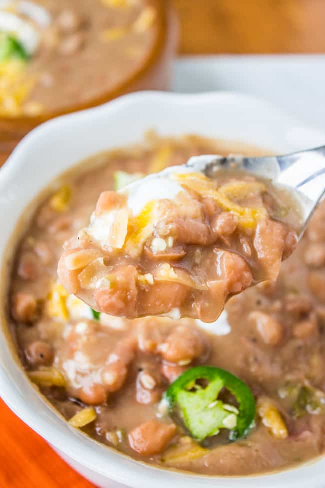 Mexican pinto beans recipe with sour cream, jalapeno, and cheddar being scooped up with a spoon.