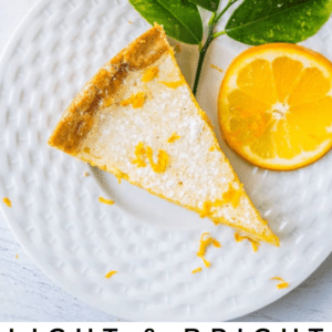 A slice of Meyer lemon tart on a white plate, garnished with lemon zest, fresh lemon, and green leaves. The text below reads: Light & Bright Meyer Lemon Tart - The Food Charlatan, featuring vibrant Meyer lemons.