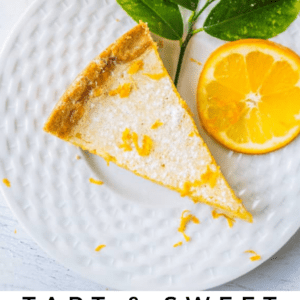 A slice of Meyer lemon tart garnished with lemon zest on a white plate, accompanied by a lemon half and green leaves. Text reads: “Tart & Sweet Meyer Lemon Tart. The Food Charlatan.” Enjoy this vibrant, citrusy delight.