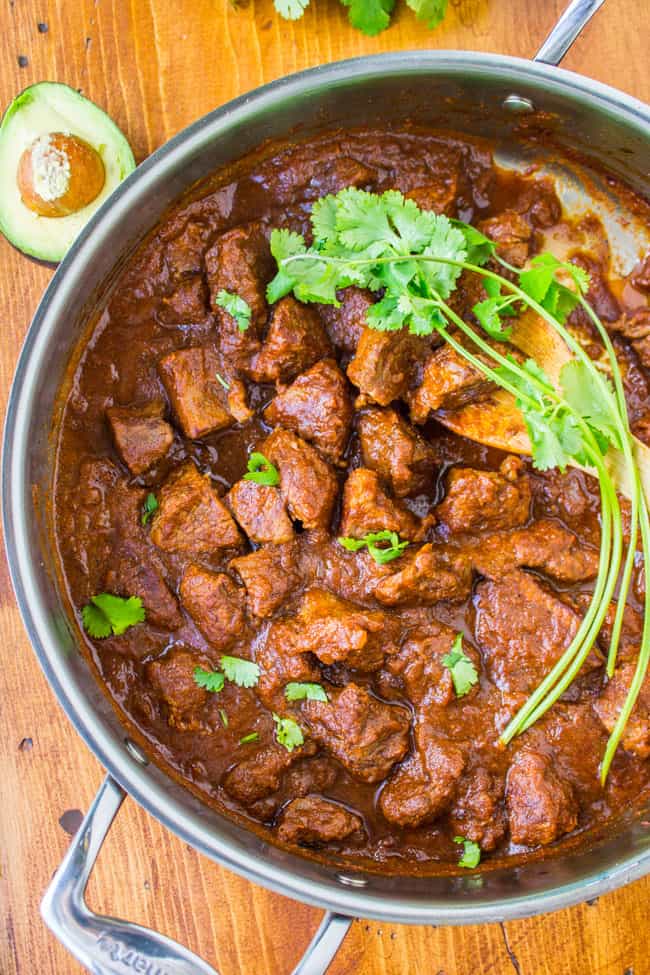 a pot of tejano carne guisada on a wooden cutting board with fresh cilantro.